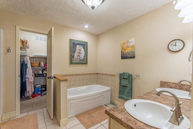 full bath with a textured ceiling, a garden tub, a sink, tile patterned floors, and a walk in closet