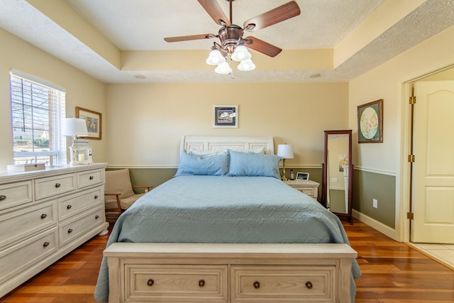 bedroom with a raised ceiling, a textured ceiling, baseboards, and wood finished floors