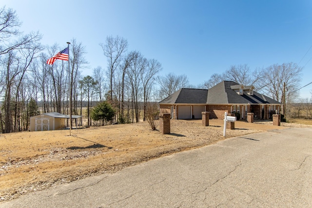 view of property exterior with brick siding, a shingled roof, a storage shed, a garage, and driveway