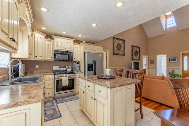 kitchen with lofted ceiling, cream cabinets, appliances with stainless steel finishes, and a sink