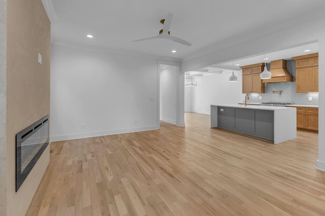 unfurnished living room with light wood finished floors, recessed lighting, a ceiling fan, a glass covered fireplace, and baseboards