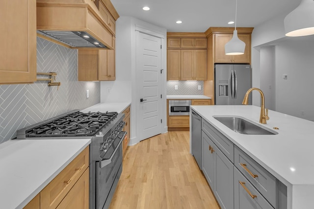 kitchen featuring light wood-style flooring, a sink, light countertops, appliances with stainless steel finishes, and custom range hood