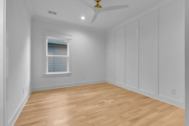 spare room with visible vents, a ceiling fan, crown molding, light wood-type flooring, and a decorative wall