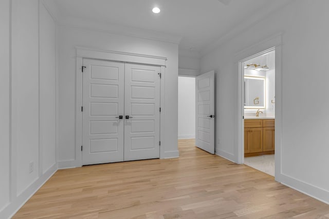 unfurnished bedroom featuring light wood finished floors, a closet, ensuite bathroom, ornamental molding, and baseboards