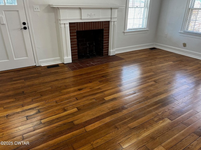 unfurnished living room featuring dark wood-style flooring, visible vents, a fireplace, and baseboards