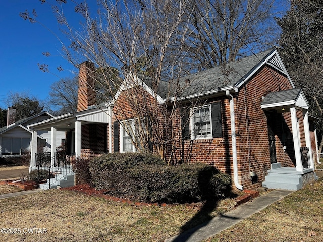 view of side of property featuring brick siding, a yard, and a chimney