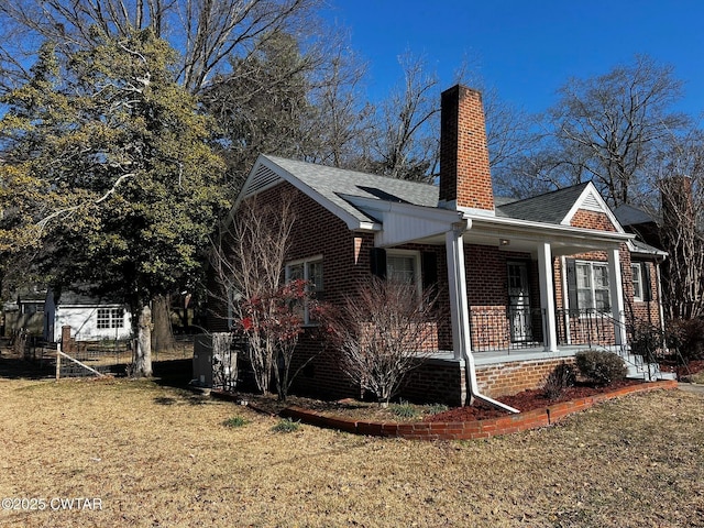 view of side of home featuring brick siding, roof with shingles, a chimney, a porch, and a lawn