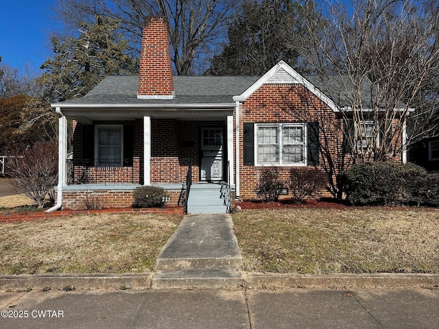 bungalow featuring covered porch, brick siding, a shingled roof, a front lawn, and a chimney