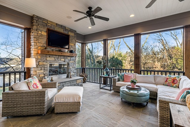 sunroom / solarium with wooden ceiling, ceiling fan, an outdoor stone fireplace, and a wealth of natural light