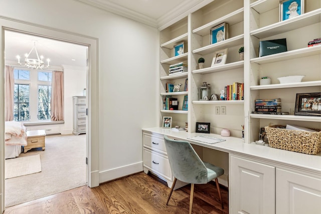 office with built in study area, crown molding, light wood finished floors, and an inviting chandelier