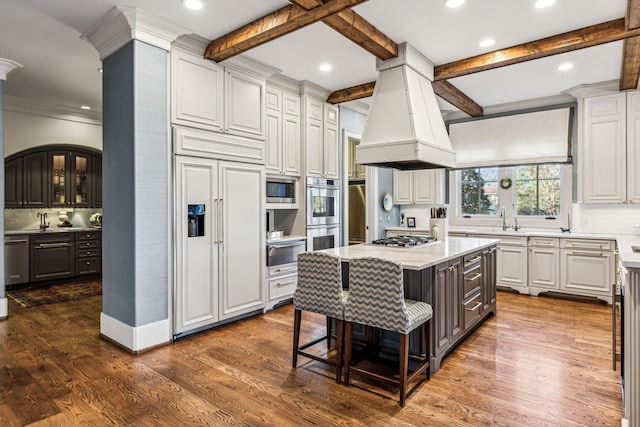 kitchen with dark wood-style floors, a kitchen island, built in appliances, premium range hood, and beam ceiling