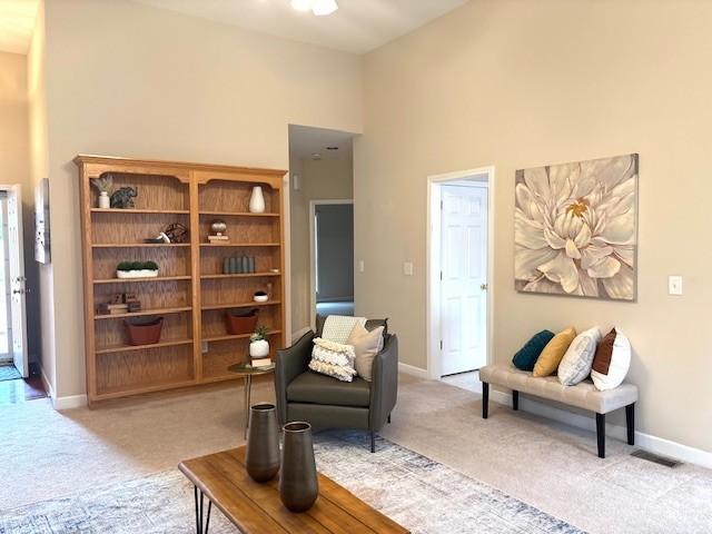 living area featuring baseboards, light colored carpet, and a towering ceiling