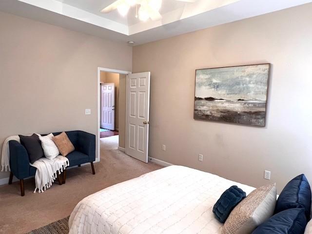 bedroom featuring light carpet, ceiling fan, a raised ceiling, and baseboards