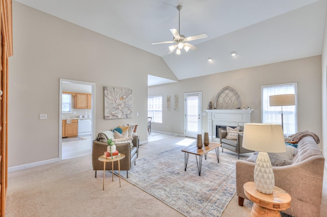 living area featuring a glass covered fireplace, ceiling fan, baseboards, and light carpet