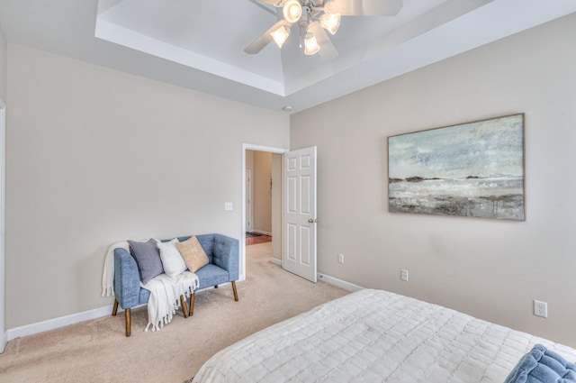 bedroom with a tray ceiling, light carpet, baseboards, and a ceiling fan