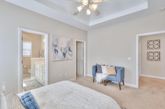 bedroom featuring a tray ceiling, light carpet, baseboards, and ensuite bathroom