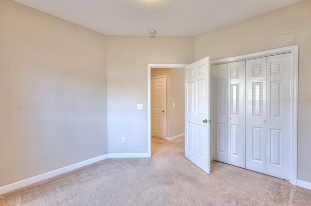 unfurnished bedroom with baseboards, light carpet, and a closet