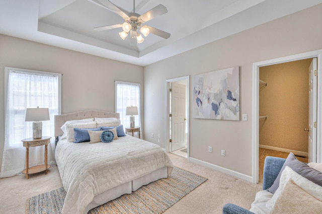 bedroom featuring a tray ceiling, baseboards, light carpet, and a spacious closet