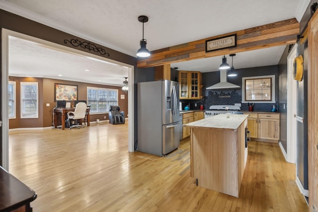 kitchen featuring glass insert cabinets, light wood-type flooring, stainless steel fridge, and wall chimney range hood