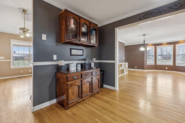 bar featuring a notable chandelier, baseboards, light wood finished floors, decorative light fixtures, and crown molding