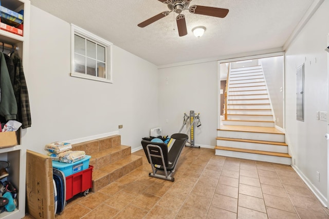 workout room featuring a textured ceiling, ceiling fan, tile patterned flooring, and baseboards