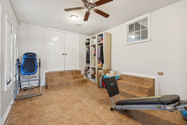 exercise area featuring visible vents, ceiling fan, a textured ceiling, and baseboards