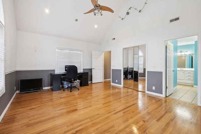 unfurnished office with visible vents, light wood-style flooring, ceiling fan, high vaulted ceiling, and baseboards