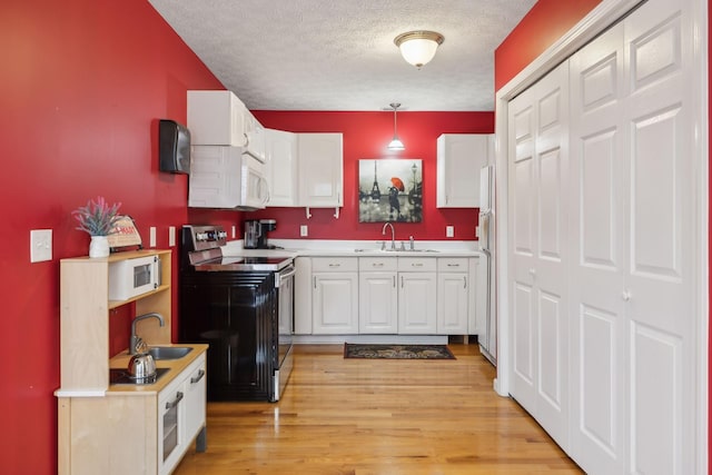 kitchen featuring white microwave, range with electric cooktop, a sink, and white cabinetry