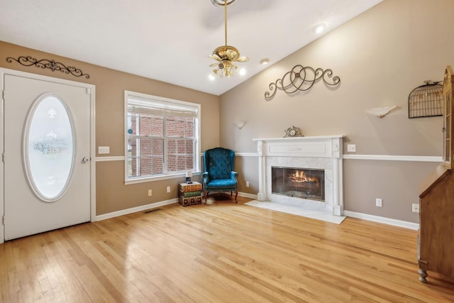 foyer entrance featuring light wood finished floors, visible vents, baseboards, lofted ceiling, and a high end fireplace