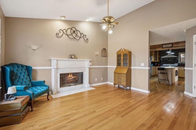 living area with a ceiling fan, light wood-type flooring, baseboards, and a premium fireplace