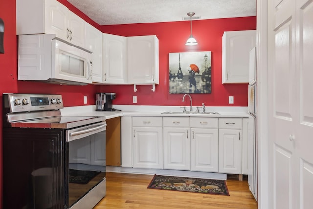 kitchen featuring electric range, a sink, white microwave, and white cabinetry