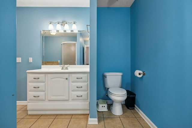 bathroom featuring baseboards, toilet, tile patterned flooring, walk in shower, and vanity