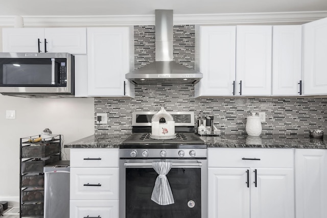 kitchen with tasteful backsplash, white cabinets, dark stone countertops, stainless steel appliances, and wall chimney range hood