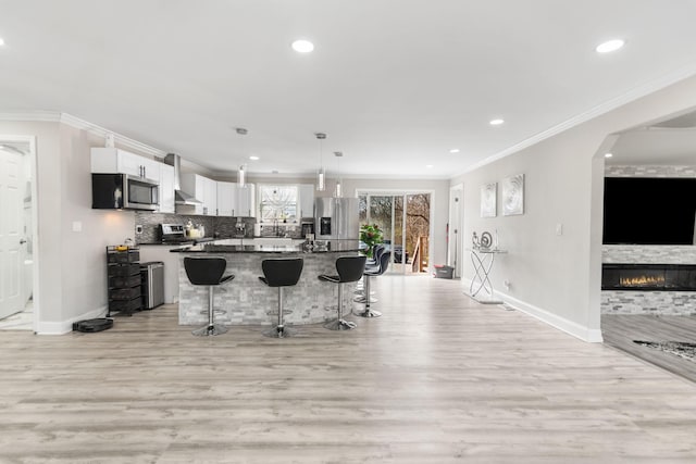 kitchen with a breakfast bar, ornamental molding, appliances with stainless steel finishes, backsplash, and wall chimney exhaust hood