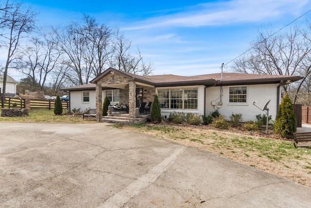 ranch-style house featuring covered porch, brick siding, and fence