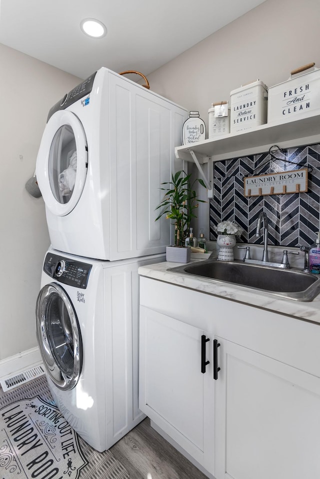 laundry room featuring stacked washer and clothes dryer, cabinet space, light wood-style floors, a sink, and baseboards