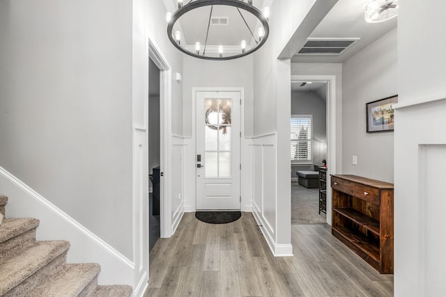 entrance foyer featuring visible vents, a notable chandelier, stairway, and wood finished floors