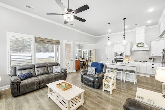 living area featuring a ceiling fan, baseboards, visible vents, light wood-style floors, and crown molding