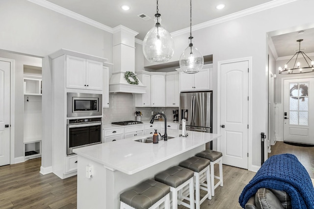 kitchen featuring stainless steel appliances, white cabinets, a sink, light wood-type flooring, and a kitchen bar