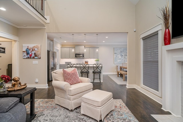 living area with a towering ceiling, dark wood-style floors, baseboards, and ornamental molding