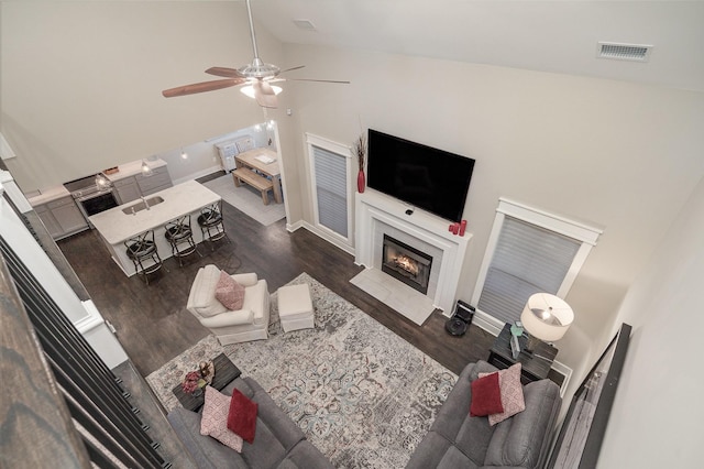 living room with high vaulted ceiling, wood finished floors, a fireplace with flush hearth, visible vents, and a ceiling fan