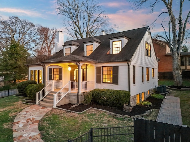 view of front facade featuring a fenced front yard, a chimney, a porch, central AC, and brick siding