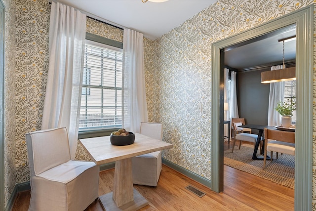 dining space featuring wallpapered walls, baseboards, visible vents, breakfast area, and wood finished floors