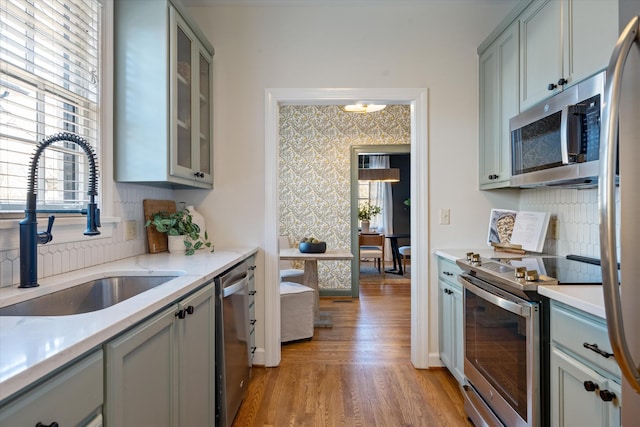 kitchen featuring wallpapered walls, gray cabinets, stainless steel appliances, and a sink