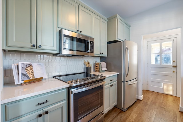 kitchen featuring light wood-type flooring, light stone counters, stainless steel appliances, and decorative backsplash