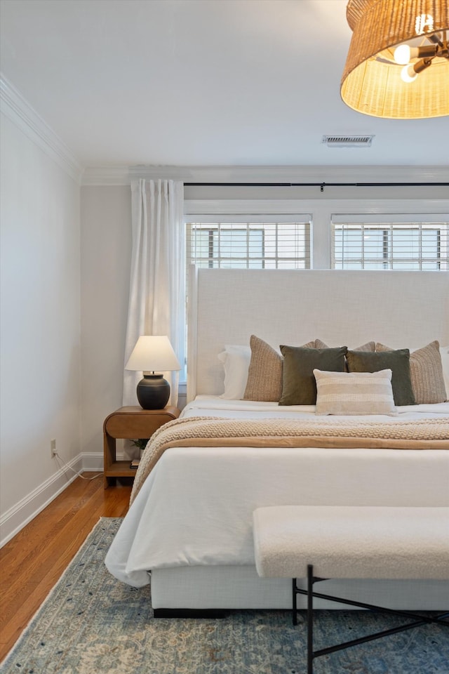 bedroom with visible vents, crown molding, baseboards, and wood finished floors