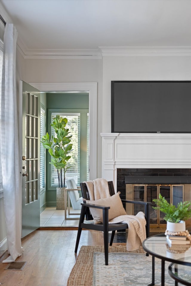 living area with ornamental molding, a glass covered fireplace, and wood finished floors