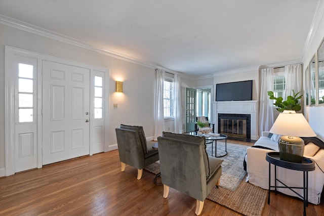 living room featuring ornamental molding, a glass covered fireplace, baseboards, and wood finished floors