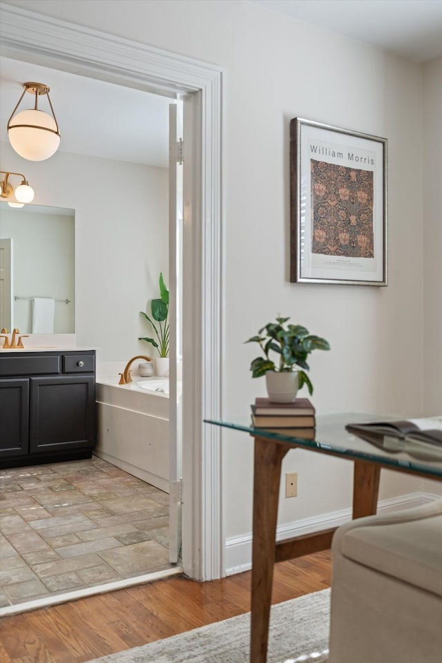 full bath with a garden tub, vanity, baseboards, and wood finished floors