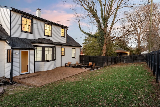 back of house at dusk featuring a fenced backyard, a chimney, a lawn, and a patio